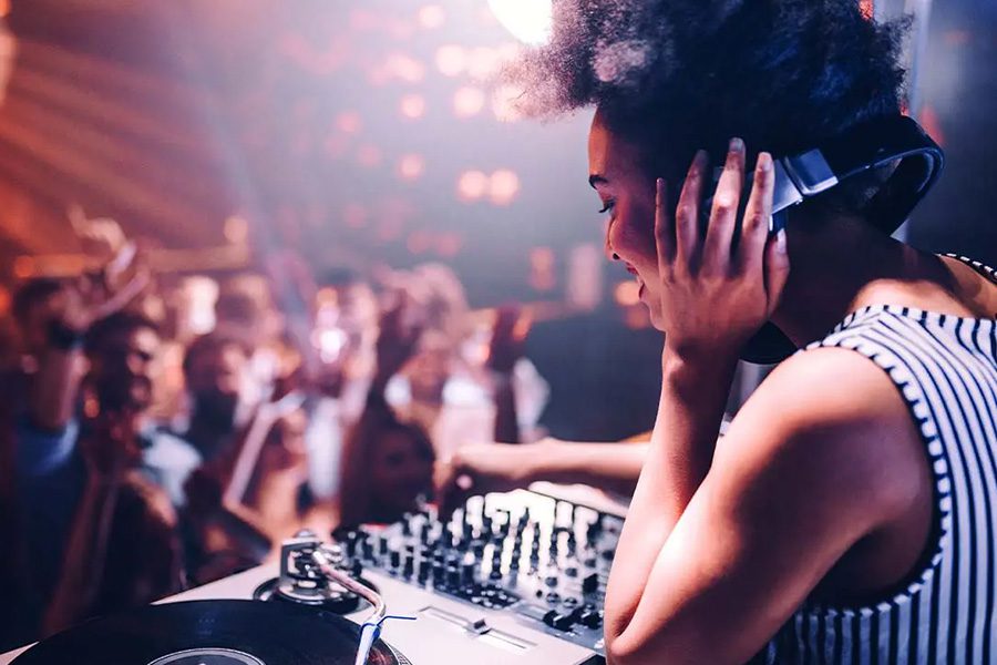 Nightclub and Bar Insurance - Focus of a DJ in a Nightclub Smiling and Listening to Her Own Beats in Front of a Large Dancing Crown with Lots of Neon Lights